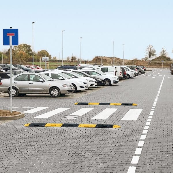 Parkplatz mit mehreren geparkten Autos, TOPSTOP-Fahrbahnschwelle 20-RE, Zebrastreifen, blaues Parkplatzschild links.