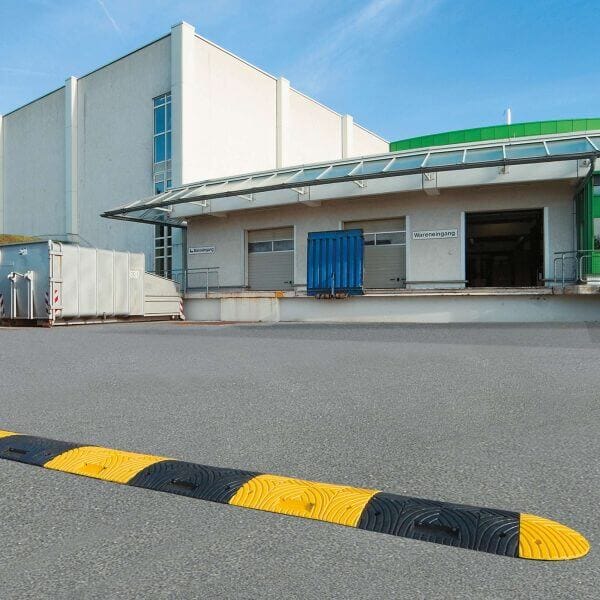 TOPSTOP-Fahrbahnschwelle vor Verladerampe eines Industriegebäudes mit Garagentoren und Metallcontainer auf dem Außengelände.