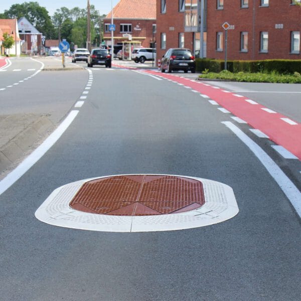 Ovales GAMMA Berliner Kissen als erhöhte Fahrbahninsel mit Profiloberfläche auf zweispuriger Stadtstraße zwischen Autos und Gebäuden.