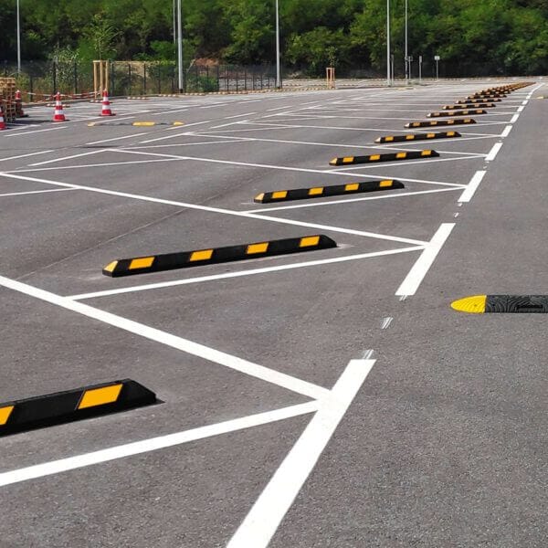 Parkplatz im Freien mit markierten Parkplätzen, Radstopp Park-AID schwarz-gelb, Verkehrskegel, Bäume im Hintergrund.