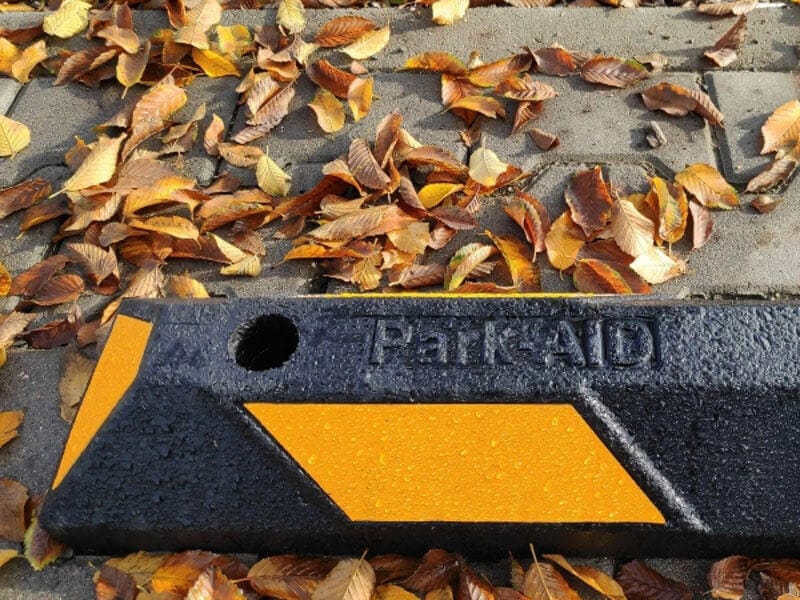 Schwarzer und gelber Radstopp Park-AID-Parkblock auf Ziegelpflaster, umgeben von braunen und gelben Herbstblättern.