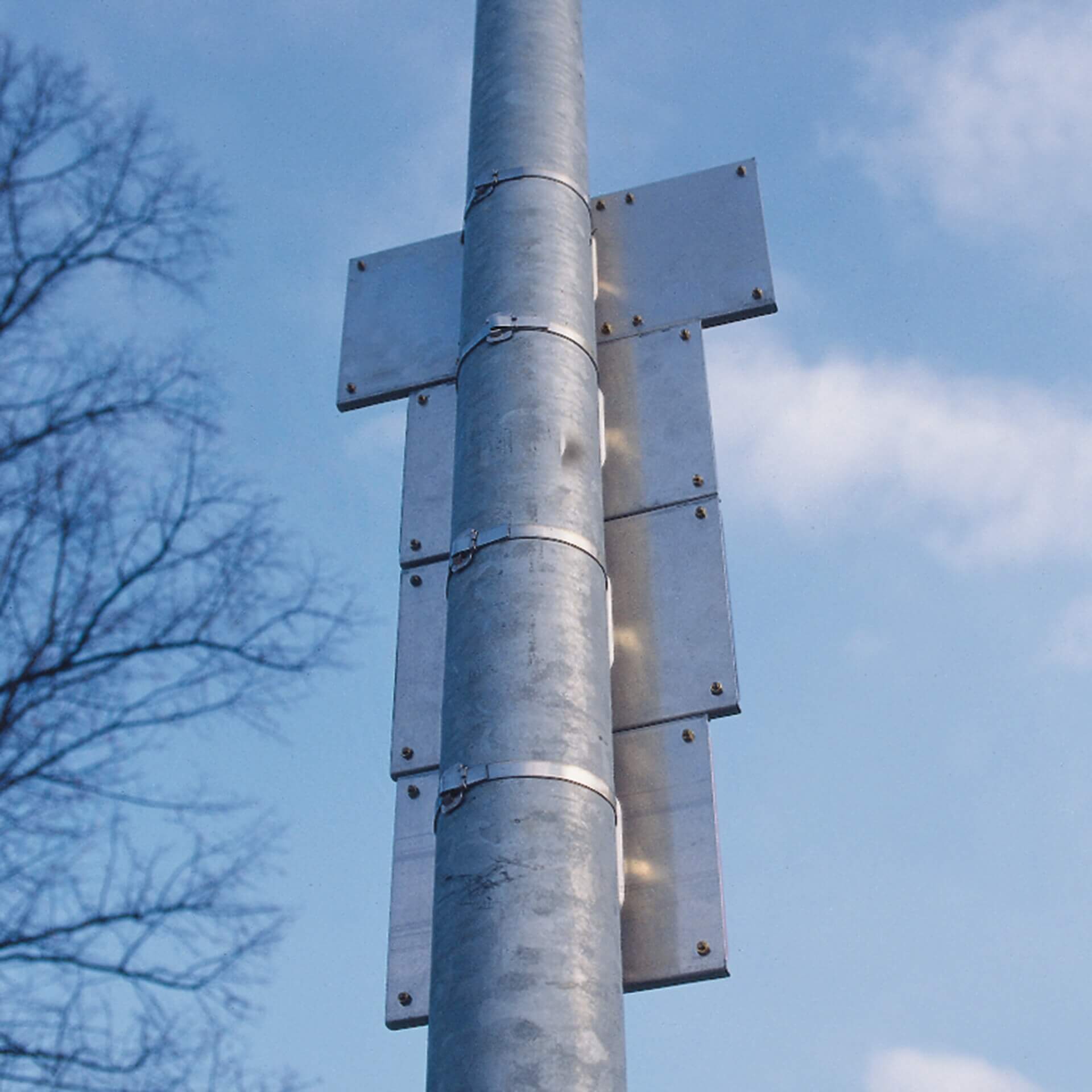 Metallpfosten mit leeren rechteckigen Metallschildern, vertikal mit Edelstahl-Band befestigt, blauer Himmel, Baumäste links.