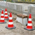 Vier orange-weiße MORION ReflexKegel stehen auf Erde neben einem Betonteil an einer Baustelle, Verkehrssicherung in Deutschland.