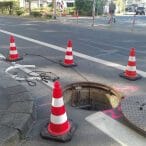 Vier MORION ReflexKegel Verkehrskegel sichern einen offenen Kanalschacht auf der Straße, Sperrung für Autos und Fußgänger.