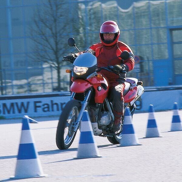 Motorradfahrer in roter Kleidung fährt auf rotem Motorrad Slalom zwischen blauen und weißen EUROPA Leitkegeln KOBOLD draußen.