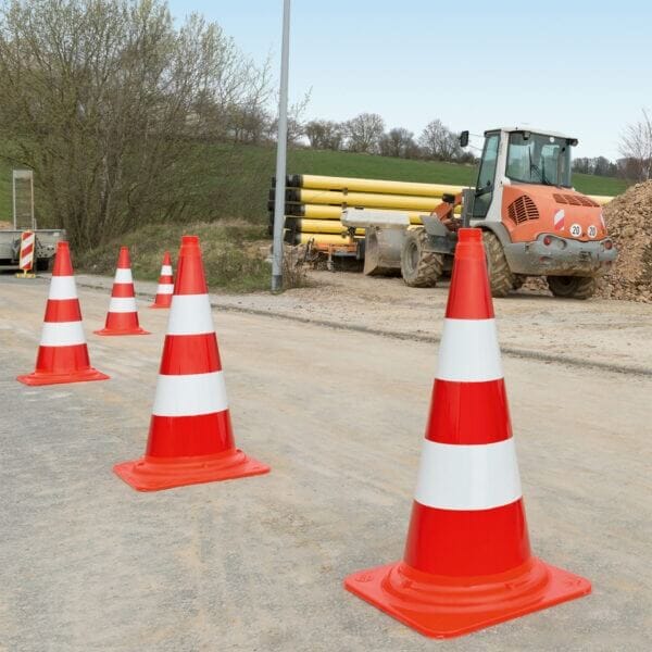 Vier MORION-Leitkegel in Orange-Weiß markieren eine Baustellen-Zufahrt mit Traktor, Rohren und Erdhügeln im Hintergrund.