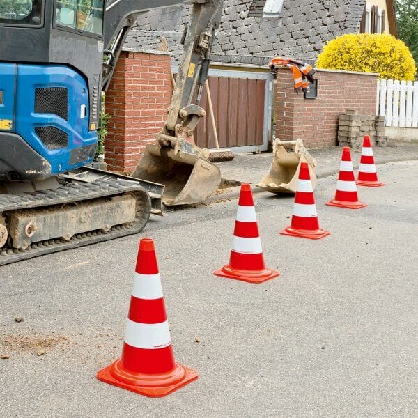 Baugerät MORION Leitkegel EU vor Backsteinmauer, fünf orange-weiße Leitkegel markieren den Rand der Baustelle an der Straße.