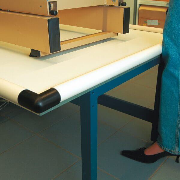 Person steht drinnen neben einem Tisch mit blauem Rahmen, schwarzen MORION Prallschutz-Ecken und Geräten auf der Tischplatte.