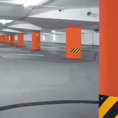 Tiefgarage mit orangen Säulen, MORION Prallschutz, schwarz-gelben Warnstreifen und freien Parkplätzen sichtbar.