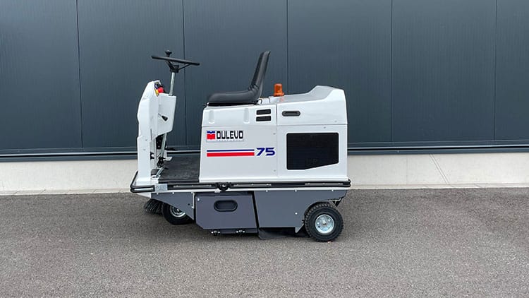Dulevo 75 Aufsitz-Kehrmaschine mit schwarzem Sitz, Lenkrad, orangem Warnlicht auf Asphalt vor dunkler Wand geparkt.