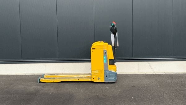 Gelber Hubwagen steht auf Asphalt vor grauer Wand, schwarzer Vogel mit roter Kappe sitzt auf dem Griff des Hubwagens.