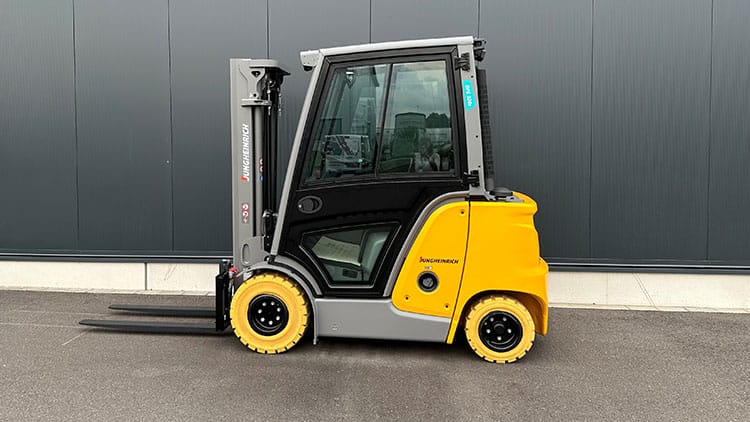 Gelber und grauer Gabelstapler steht auf Asphalt vor einer dunkelgrauen Metallwand.