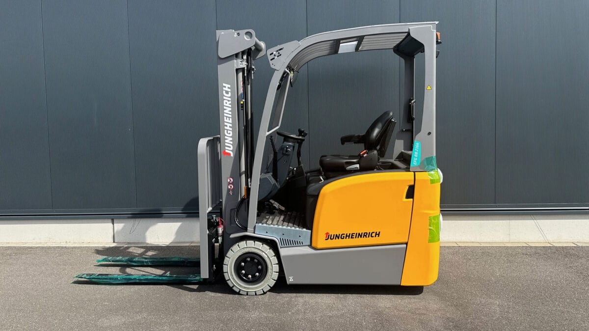 Gelber und grauer Jungheinrich Gabelstapler steht draußen auf Pflaster vor dunkler Wand. Industrie, Lagerlogistik, Flurförderzeug.