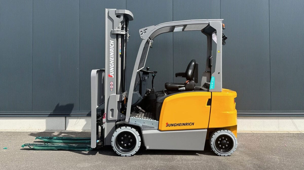 Gelber und grauer Jungheinrich Gabelstapler steht auf Asphalt vor dunkler grauer Wand, Industriemaschine, Logistik.