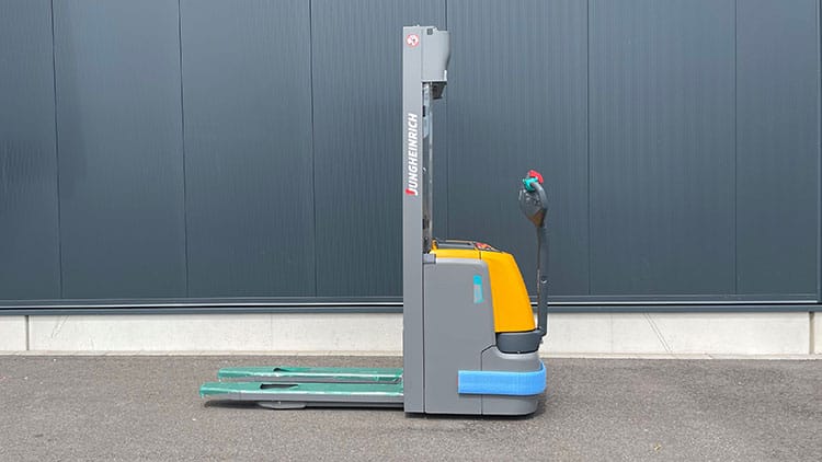 Seitenansicht eines industriellen Elektrohubwagens auf Asphalt vor einer dunkelgrauen Wand, Gabeln sichtbar.