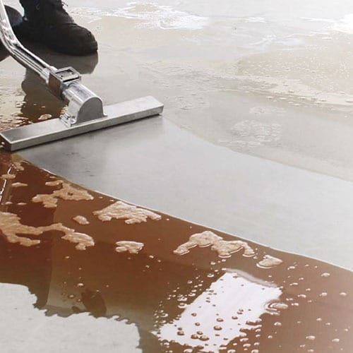 Eine Person saugt mit einem Nasssauger eine braune Flüssigkeit von einem glatten, hellen Boden auf.