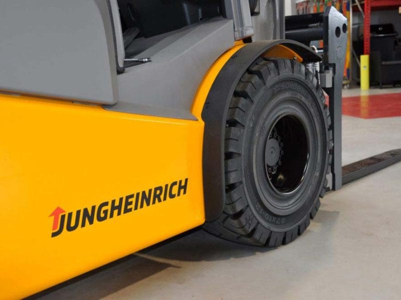 Detailaufnahme eines gelben Jungheinrich Gabelstaplers, Schwerpunkt Vorderrad und Gabelzinken auf Lagerhausboden.