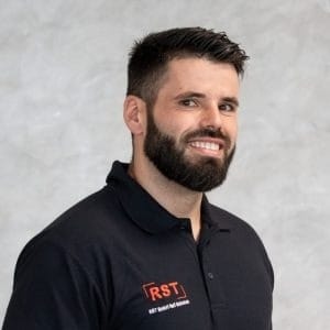 Mann mit kurzem grauem Haar lächelt, trägt dunkles Hemd vor hellem Hintergrund; Porträt für Technische Industrieberatung.